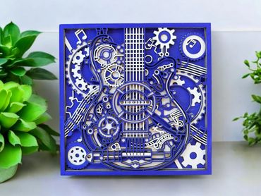 Intricate blue and white layered paper art of a guitar with gears and musical notes.