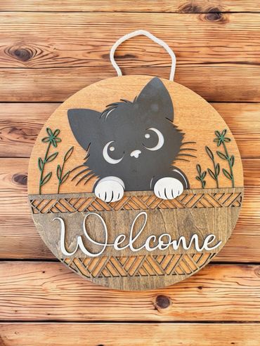 Cute wooden welcome sign featuring a playful black cat and flowers.