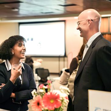 Two professionals smiling and talking in an office setting.