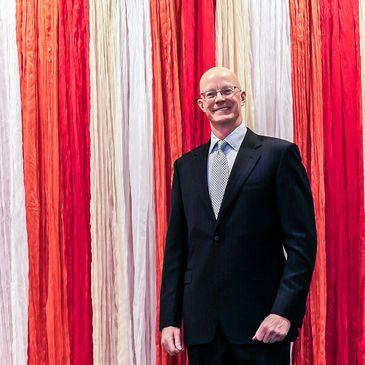 Man in suit standing against red and white striped background.