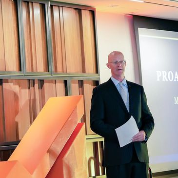 Man in suit giving a presentation with screen and wooden decor.