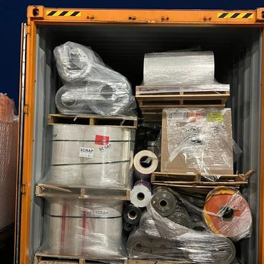 A shipping container filled with wrapped rolls and pallets labeled as scrap.
