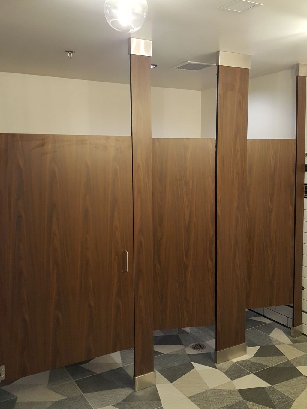 Floor to ceiling mounted solid phenolic partitions in a public restroom.