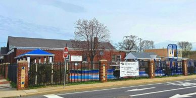 Exterior view of a preschool with playground and fence on a cloudy day.