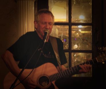 Man singing and playing guitar indoors in dim lighting.
