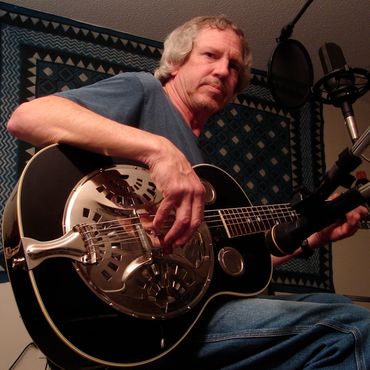 Man playing a resonator guitar with microphones in a cozy room.