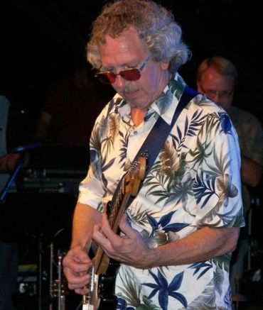 Man in floral shirt playing electric guitar on stage.