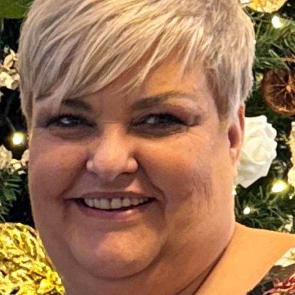 Smiling woman with short blonde hair in front of festive decorations.
