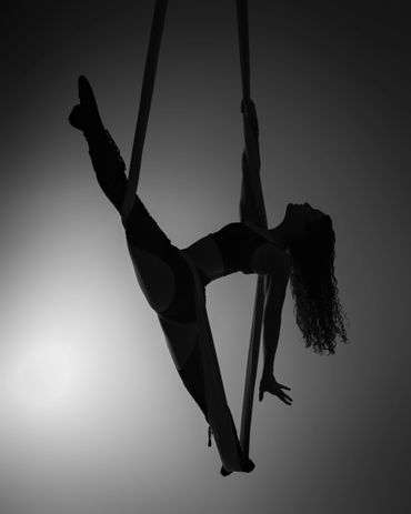 Silhouette of a woman gracefully performing aerial silk acrobatics.
