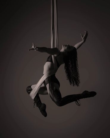 Aerial dancer gracefully suspended mid-air with flowing hair and dramatic pose.