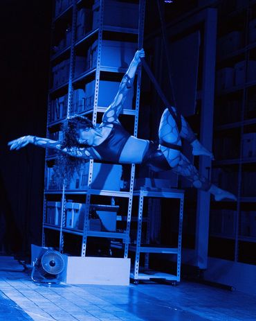 Aerial dancer performing on a hoop in a blue-lit studio.