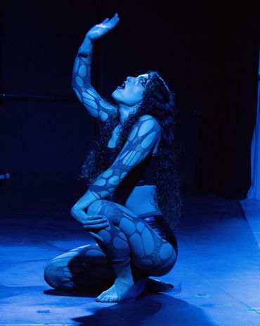 Dancer in patterned bodysuit illuminated by blue light, striking a graceful pose.