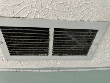 Dusty and cobweb-filled ceiling vent in a textured ceiling room.
