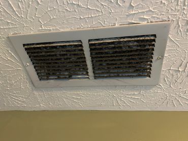 Dirty ceiling air vent covered in dust and cobwebs.