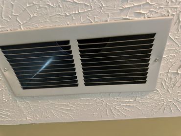 Close-up of a white ceiling air vent with textured ceiling.