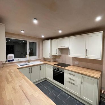 Modern kitchen with white cabinets and wooden countertops under recessed lighting.