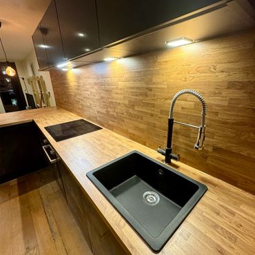 Modern kitchen with wooden countertops, black sink, and sleek lighting.