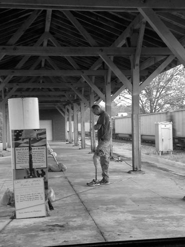 Man with a prosthetic leg stands solemnly at a memorial under a covered platform.