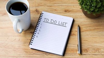A to-do list, pen, coffee cup and plant on a desk.
