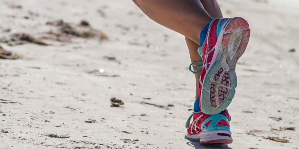 Person running on sandy beach wearing bright running shoes.