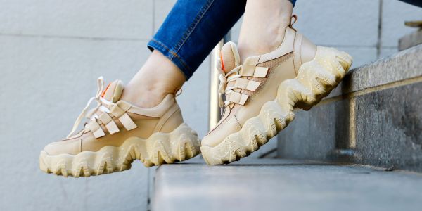 Beige chunky sneakers on feet near steps.