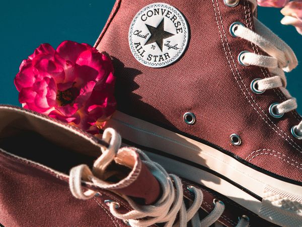 Close-up of maroon Converse sneakers with a bright pink flower.