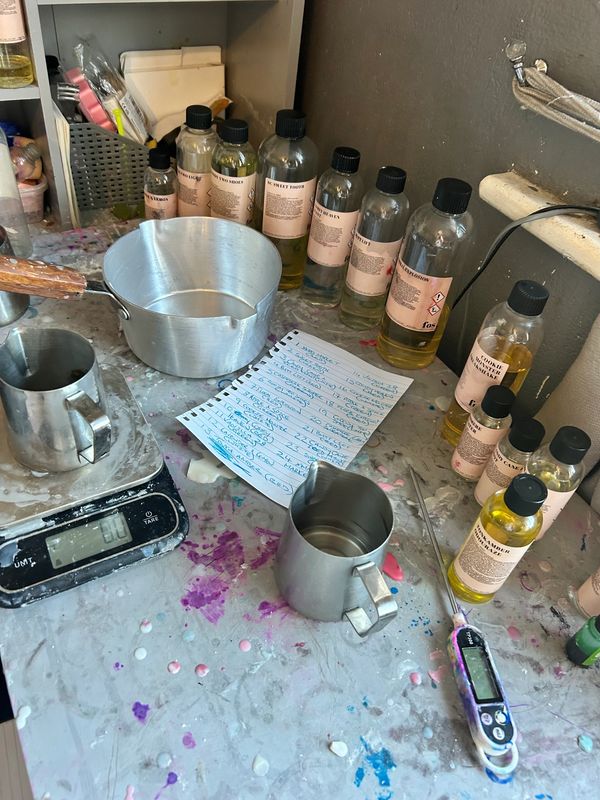 Workspace with bottles, metal containers, a scale, and a handwritten list on a paint-splattered table.