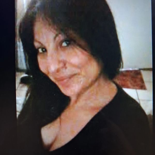 Smiling woman with long dark hair in a dimly lit room.