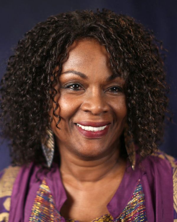 Smiling woman with curly hair wearing colorful clothing and earrings.