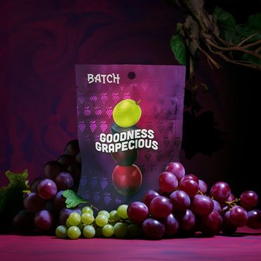 A colorful packet labeled 'Goodness Grapecious' surrounded by fresh green and red grapes.