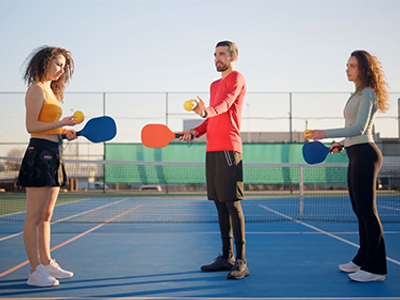 Three people holding paddles and balls on a pickleball court.