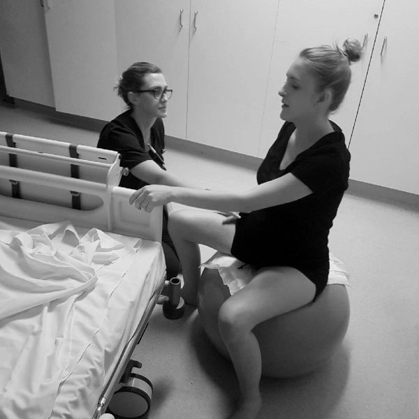 Two women in a hospital room, one on an exercise ball.