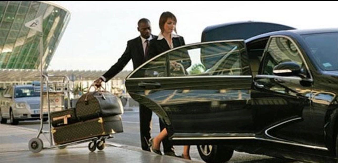 A woman entering a black luxury car with a man carrying her luggage.