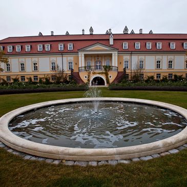 Elegant historical building with a circular fountain in front and manicured lawns.