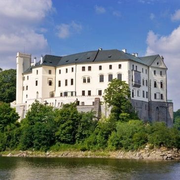 A large white castle on a forested island surrounded by water under a partly cloudy sky.