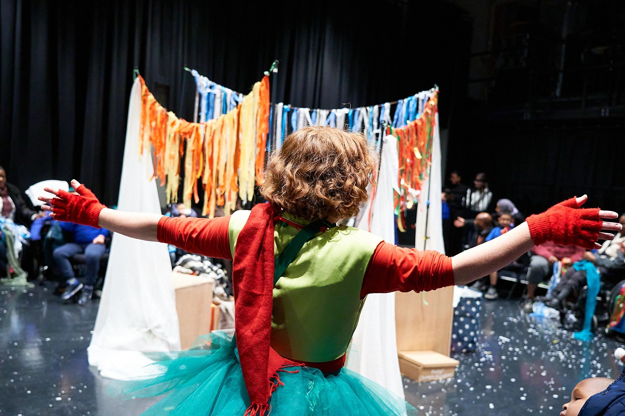 Robyn stands in front of an audience, her arms outstretched. The floor is covered in snow.