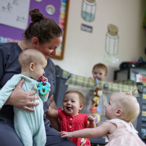 An educator holds a baby while smiling at other small children.