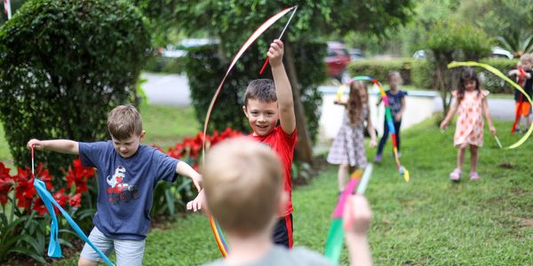 Young children play outside with outside learning. They are twirling ribbons. 