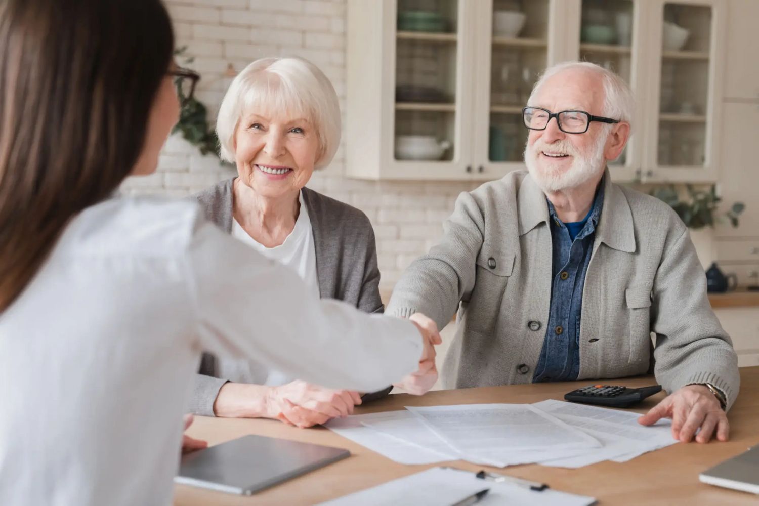 Elderly couple shaking hands with a professional in a home setting.