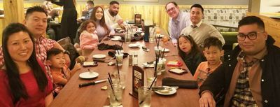 Large family and friends gathered around a restaurant table, smiling and enjoying time together.