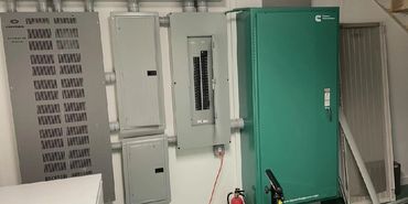 Electrical panels and a large green power system unit in a basement room.