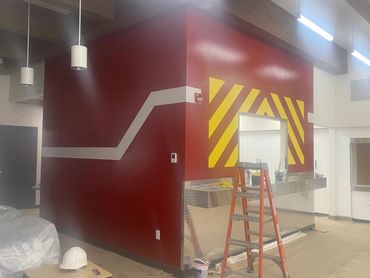 Interior view of a room under construction with red and yellow wall designs and a ladder.