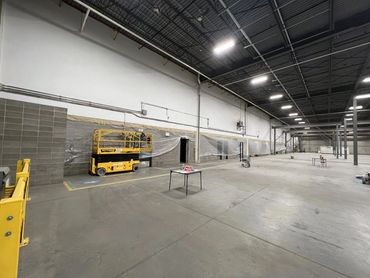 Spacious industrial warehouse with construction equipment and protective plastic sheeting along walls.