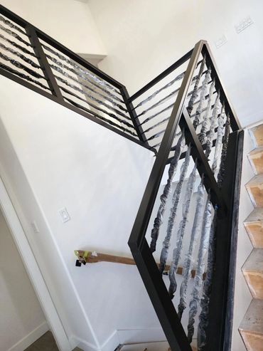 Modern black metal stair railing with protective wrapping on balusters.