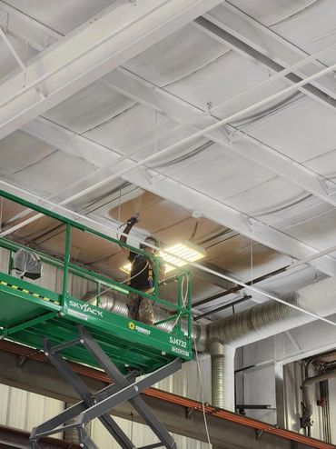 Worker on a green Skyjack lift painting a ceiling in an industrial space.