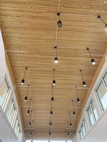 Modern wooden ceiling with hanging black pendant lights and windows on both sides.