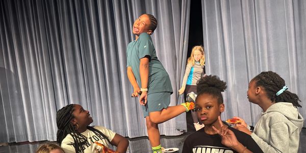 Kids posing and eating on stage with a gray curtain backdrop.