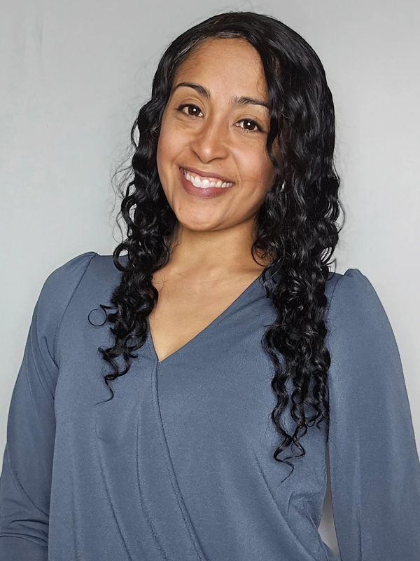 Smiling woman with curly hair wearing a blue top against a plain background.
