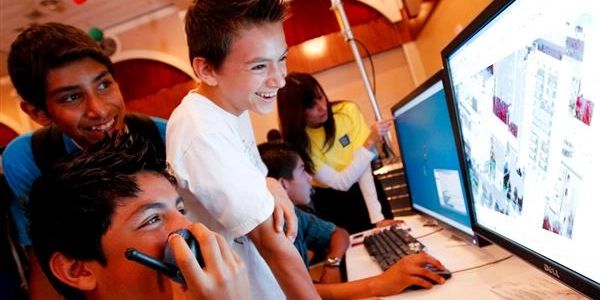 Photograph of 3 children smiling at something on a compter screen (can't really see what is on the s