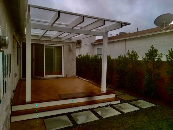 Modern backyard deck with white pergola and glowing blue step lights.